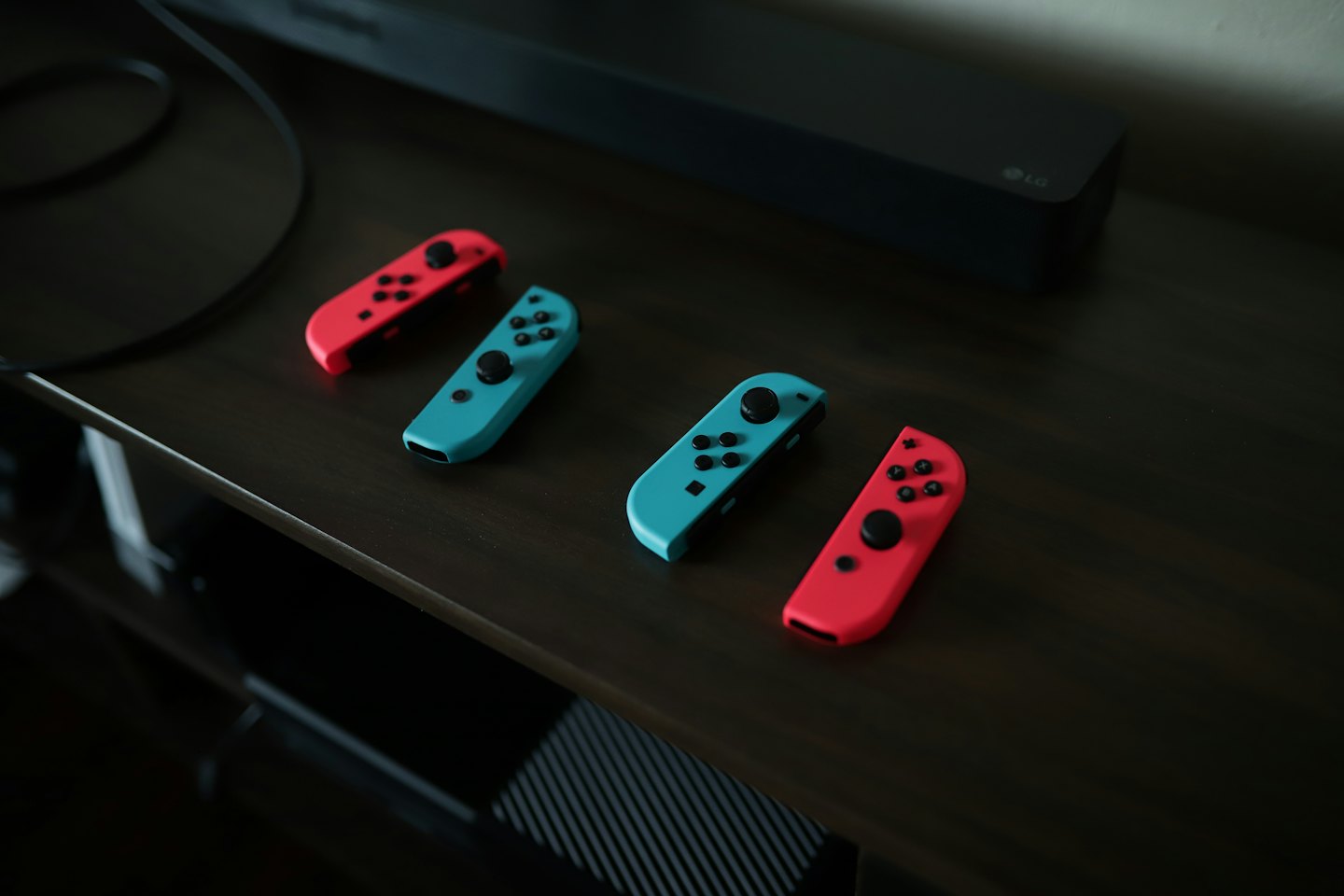Four gaming controllers arranged on a wooden shelf.